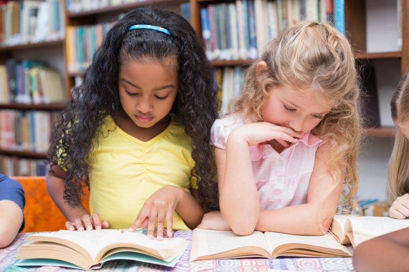 two elementary aged girls reading books side by side