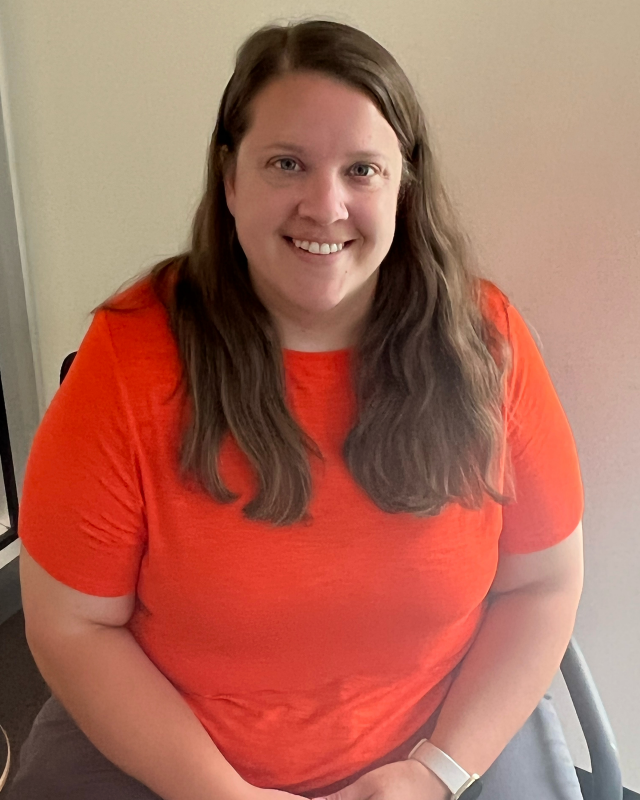 woman with long brown hair wearing orange shirt smiling