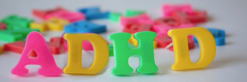 Pink, yellow, and green plastic magnetic letters arranged to spell ADHD