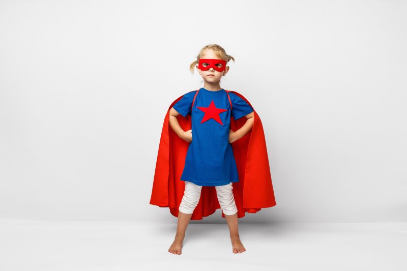 Little girl dressed up with a superhero cape and mask