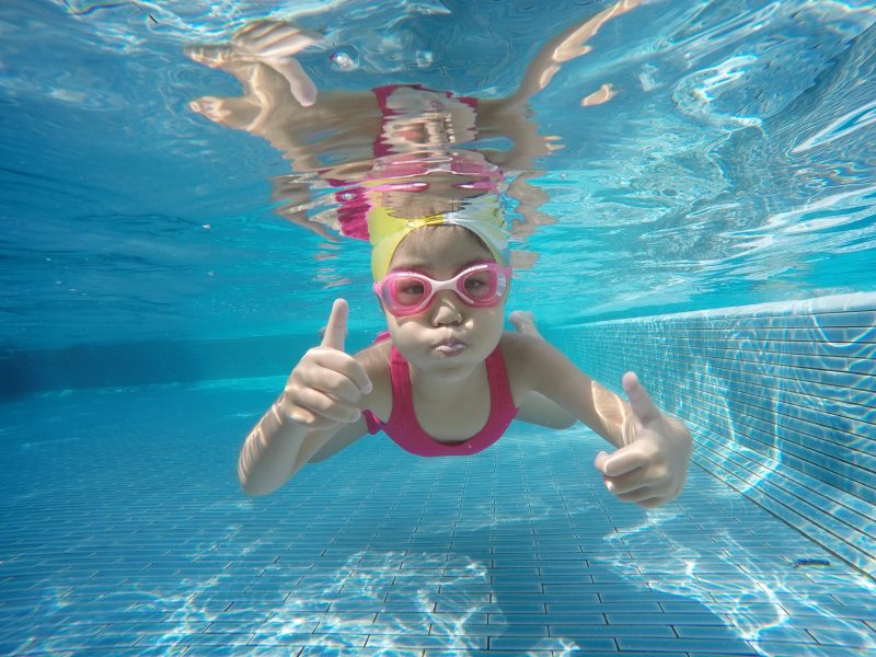 Small girl swimming underwater giving a thumbs up